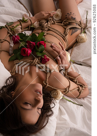 Sensual naked woman tied with ropes lying on bed 92625088