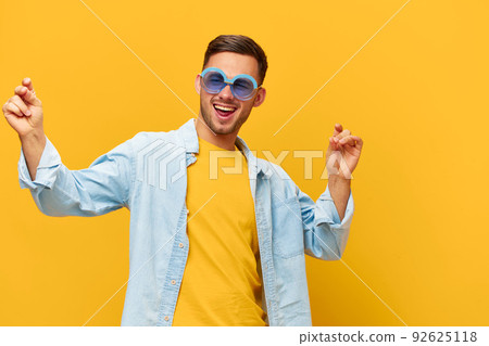 Dancing joyful tanned handsome man in blue shirt trendy sunglasses raise hands up posing isolated on orange yellow studio background. Copy space Banner Mockup. Relax time Party concept Dancing joyful tanned handsome man in blue shirt trendy sunglasses raise hands up posing isolated on orange yellow studio background. Copy space Banner Mockup. Relax time Party concept 92625118