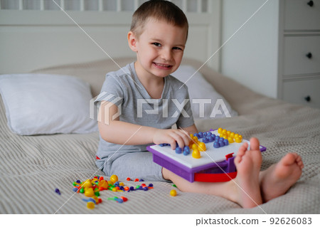Little happy caucasian boy in a light room on the bed collects color mosaic to creating images 92626083