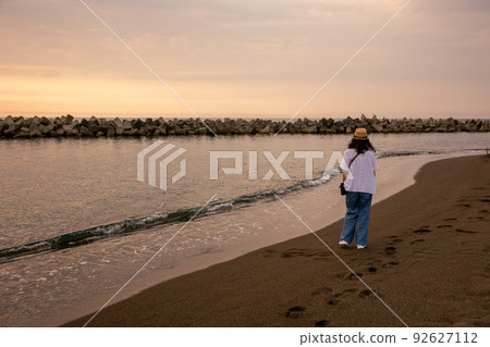 A woman standing in the quiet sea at sunset 92627112