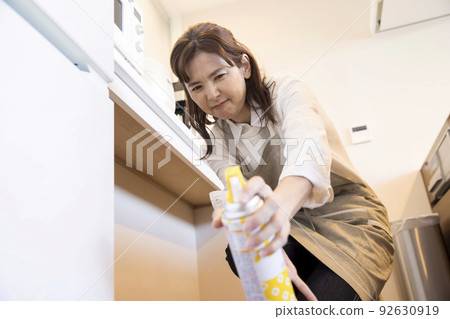 Middle woman using insecticide for cockroaches in the kitchen 92630919