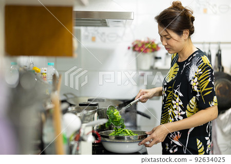 An authentic real shot of Asian woman boiling and cooking green vegetables for food in kitchen. 92634025