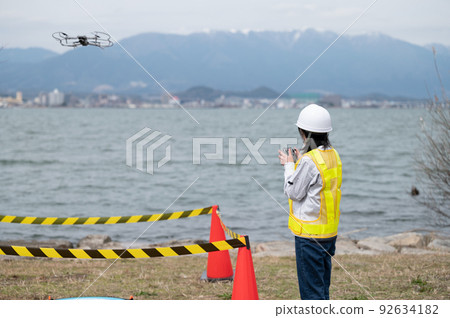 Young female worker operating a drone at a construction site and taking photos Young female worker operating a drone at a construction site and taking photos 92634182