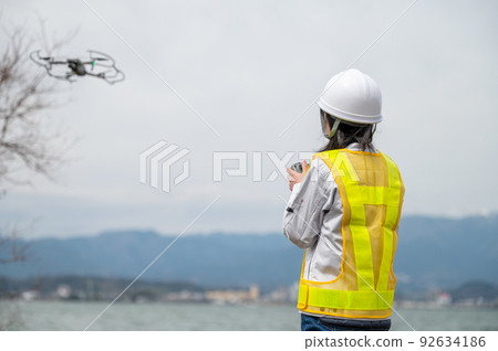 Young female worker operating a drone at a construction site and taking photos Young female worker operating a drone at a construction site and taking photos 92634186