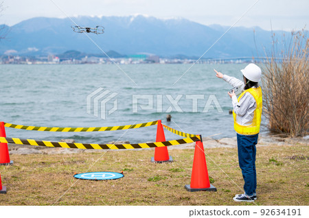 Young female worker operating a drone at a construction site and taking photos 92634191