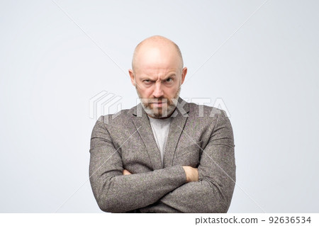 Portrait of offended european man in suit holding hands crossed on chest, looking from under forehead Portrait of offended european man in suit holding hands crossed on chest, looking from under forehead 92636534