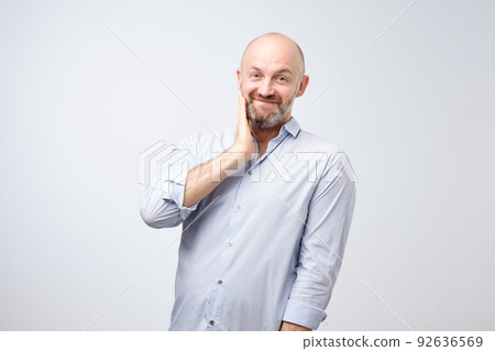Pleasant charming european male with beard bring hands towardfacewith lovely expression as if receiving compliment Pleasant charming european male with beard bring hands towardfacewith lovely expression as if receiving compliment 92636569
