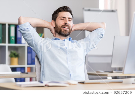 Young handsome man, office worker, sitting at a computer desk, stretching, tired, taking a break, doing yoga exercises, resting 92637209