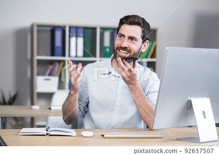 Cheerful and happy man records audio messages, freelance businessman in office, uses application on smartphone 92637507