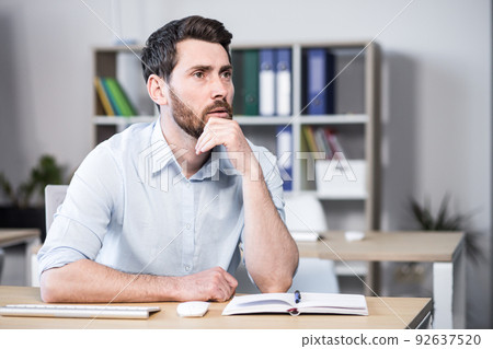 Close up photo. Upset, tired and thoughtful young man, office worker, manager, freelancer. He holds his head in his hands. Sitting at a computer desk in the office Close up photo. Upset, tired and thoughtful young man, office worker, manager, freelancer. He holds his head in his hands. Sitting at a computer desk in the office 92637520