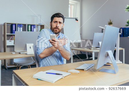 Businessman works during the day in a modern bright office, a man coldly holds a remote control from the air conditioner, raises the temperature 92637669
