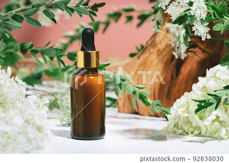 Amber glass dropper bottle of serum or oil in nature. Leaves and flowers on pink 92638030