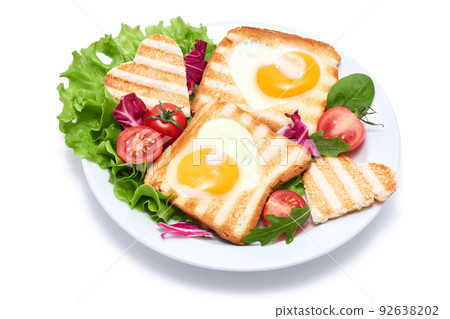 Fried egg Toasts with heart shaped holes on white ceramic plate Fried egg Toasts with heart shaped holes on white ceramic plate 92638202