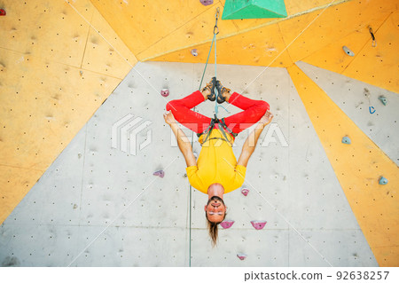 A man hangs upside down in a lotus position on a climbing wall A man hangs upside down in a lotus position on a climbing wall 92638257