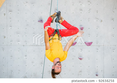 A man hangs upside down in a lotus position on a climbing wall 92638258