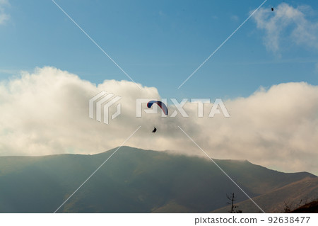 Paraglider flying over clouds in summer day Paraglider flying over clouds in summer day 92638477