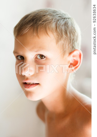 A cute young cheerful blond boy with a natural smile smiles happily while standing against a light beige background with bare shoulders. A cute young cheerful blond boy with a natural smile smiles happily while standing against a light beige background with bare shoulders. 92638634