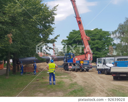 Laying heating pipes in a trench at construction site.  92639028