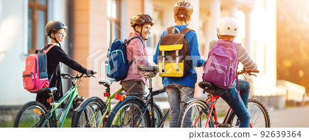 Children with rucksacks riding on bikes in the park near school 92639364