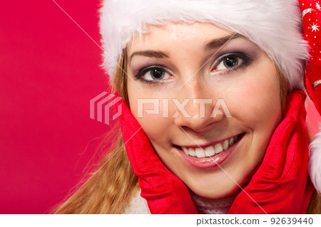 Beautiful young woman in santa claus hat and mittens smiling. Christmas tale. Red background. Postcard. Space for text. Beautiful young woman in santa claus hat and mittens smiling. Christmas tale. Red background. Postcard. Space for text. 92639440