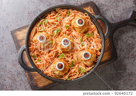 Scary Halloween food of meatballs with monster eyes and pasta with tomato sauce in a pan on the table close-up. Horizontal top view Scary Halloween food of meatballs with monster eyes and pasta with tomato sauce in a pan on the table close-up. Horizontal top view 92640172