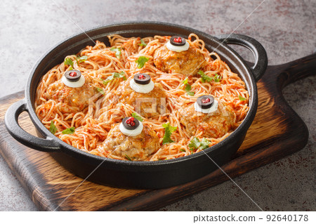 Halloween dinner of meatballs with monster eyes and pasta with tomato sauce in a frying pan close-up. Horizontal 92640178