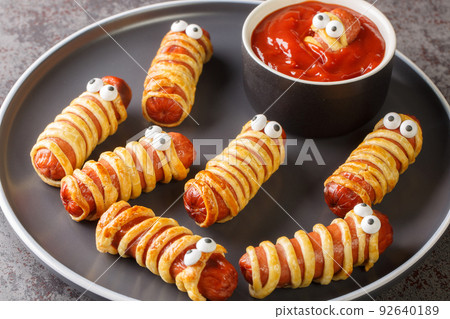 Homemade sausage mummies with ketchup Halloween funny food recipe closeup in the plate. Horizontal Homemade sausage mummies with ketchup Halloween funny food recipe closeup in the plate. Horizontal 92640189