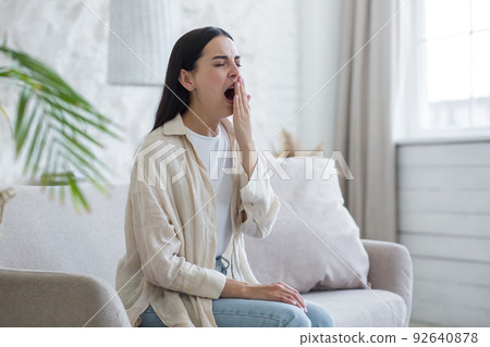 Beautiful woman at home sitting on the sofa tired yawning, sleepless brunette 92640878