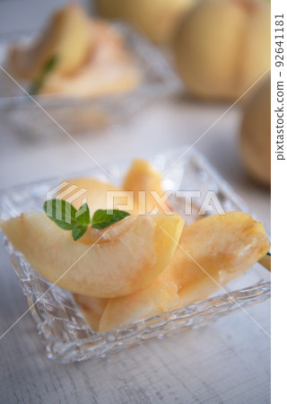 Pieces of japanese white peach in glass bowl on wooden background. Pieces of japanese white peach in glass bowl on wooden background. 92641181