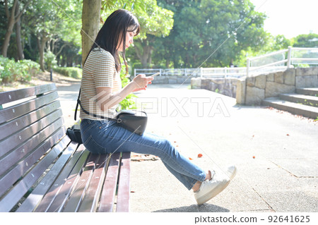 A woman operating a smartphone on a park bench 92641625