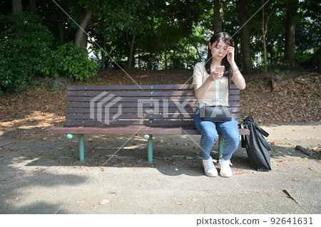 A woman operating a smartphone on a park bench 92641631