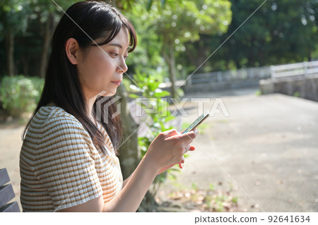 A woman operating a smartphone on a park bench 92641634