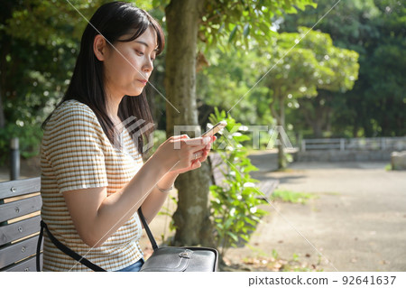 A woman operating a smartphone on a park bench 92641637
