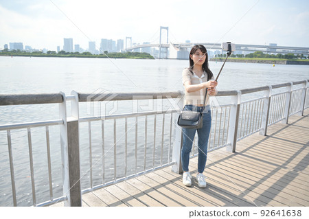 A woman taking a picture with a smartphone using a selfie stick at the beach 92641638