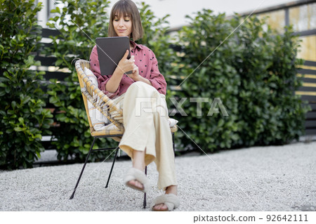 Woman working on digital tablet while sitting relaxed at backyard Woman working on digital tablet while sitting relaxed at backyard 92642111