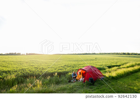Couple and pet at campsite with tent on a green field 92642130