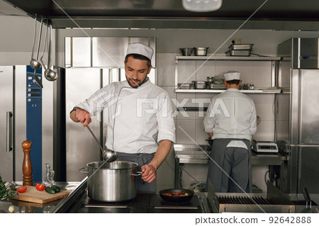 Chef cooking tasty dish in kitchen of restaurant using modern equipment Chef cooking tasty dish in kitchen of restaurant using modern equipment 92642888