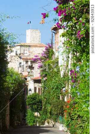 Grimaldi castle tower in Antibes city center from a flowered narrow street 92643913