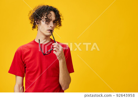 Incredulous myopic young student man in red t-shirt hold funny eyewear on teeth posing isolated on yellow studio background. The best offer with free place for advertising. Education College concept Incredulous myopic young student man in red t-shirt hold funny eyewear on teeth posing isolated on yellow studio background. The best offer with free place for advertising. Education College concept 92643958