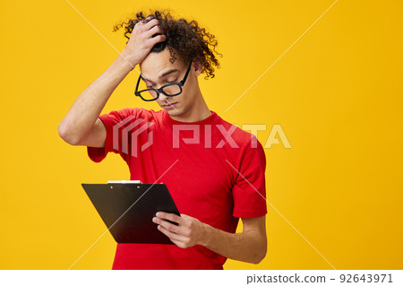 Thoughtful myopic young student man in red t-shirt funny eyewear holds tablet folder with study notes posing isolated on over yellow studio background. Free place for ad. Education College concept 92643971