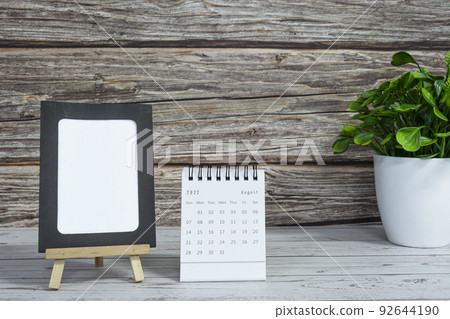 White August 2022 calendar on wooden desk with paper frame and potted plant. White August 2022 calendar on wooden desk with paper frame and potted plant. 92644190