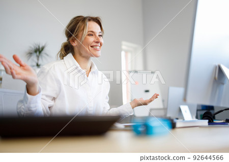 Pleasant business woman talking on video call while sitting at workplace in office 92644566