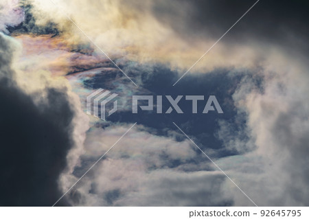 Diffraction of light on drops of supercooled water in clouds, rainbow clouds against the blue sky in clear sunny weather, irisation of cumulus clouds, optical phenomenon, spectral colors Diffraction of light on drops of supercooled water in clouds, rainbow clouds against the blue sky in clear sunny weather, irisation of cumulus clouds, optical phenomenon, spectral colors 92645795