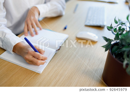 Close-up view of a woman's hand with a pen writes in a notebook 92645979