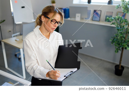 Serious business woman writing on clipboard in office 92646011