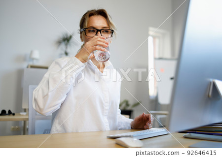 Beautiful mature business woman working at a computer and drinking glass of fresh water Beautiful mature business woman working at a computer and drinking glass of fresh water 92646415