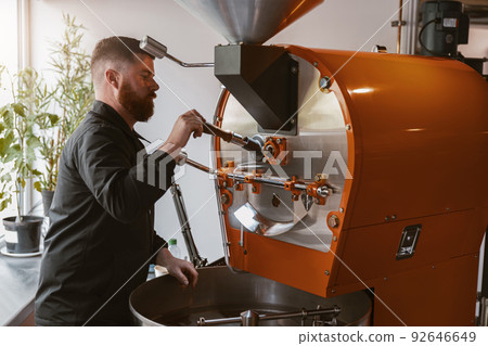 Business owner operating modern coffee bean roasting machine at manufacturing Business owner operating modern coffee bean roasting machine at manufacturing 92646649