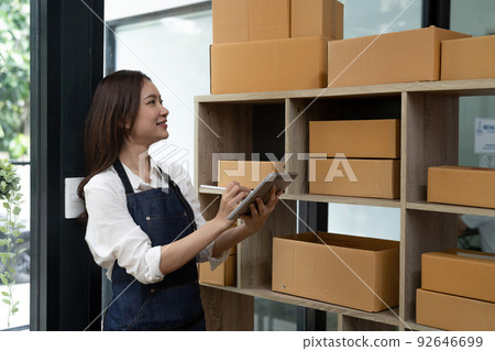 Asian female entrepreneur checking orders to arrange the produce before packing the products in the inner boxes with the customers. Freelance concepts Asian female entrepreneur checking orders to arrange the produce before packing the products in the inner boxes with the customers. Freelance concepts 92646699