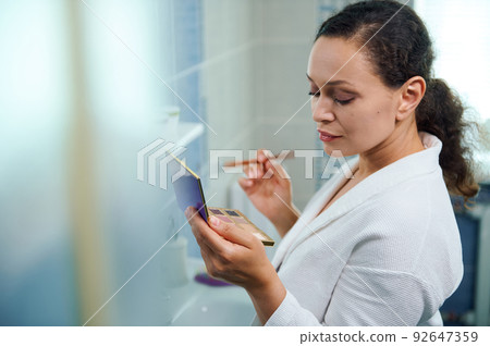 Side view. Pretty woman holding a make-up brush and a fashionable colorful eyeshadows palette, standing in the bathroom 92647359