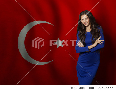 Cheerful young woman in blue dress smiling against Turkish flag background Cheerful young woman in blue dress smiling against Turkish flag background 92647367